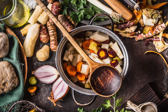 Wurzelgemüse-Suppe mit Kurkuma und Ceyennepfeffer in einem kleinen Topf auf dem ein Kochlöffel aus Holz liegt umgeben von viel Wurzelgemüse