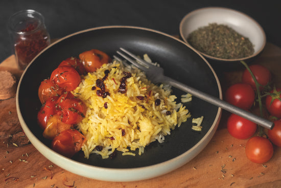 Persischer Safranreis mit Essigbeeren auf einem dunklen Teller zusammen mit Thymian Tomaten auf einem Holzbrett 