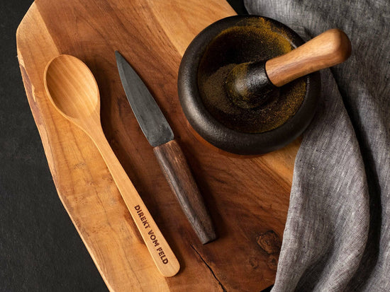 Kochlöffel aus Kirschholz auf Holzbrett mit Messer und Mörser
